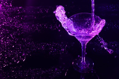 Photo of Pouring martini. Glass and splashes in neon lights on dark background, space for text