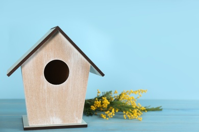 Beautiful bird house and mimosa flowers on wooden table against light blue background, space for text