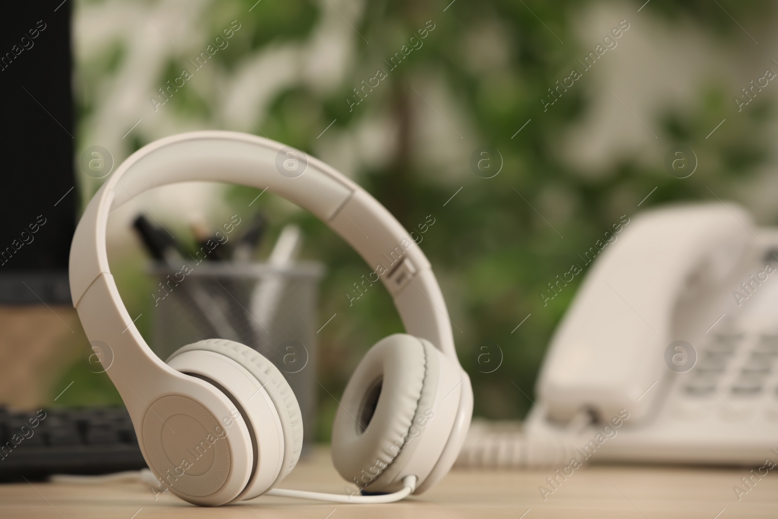 Photo of Modern headphones, desktop telephone and computer on table indoors