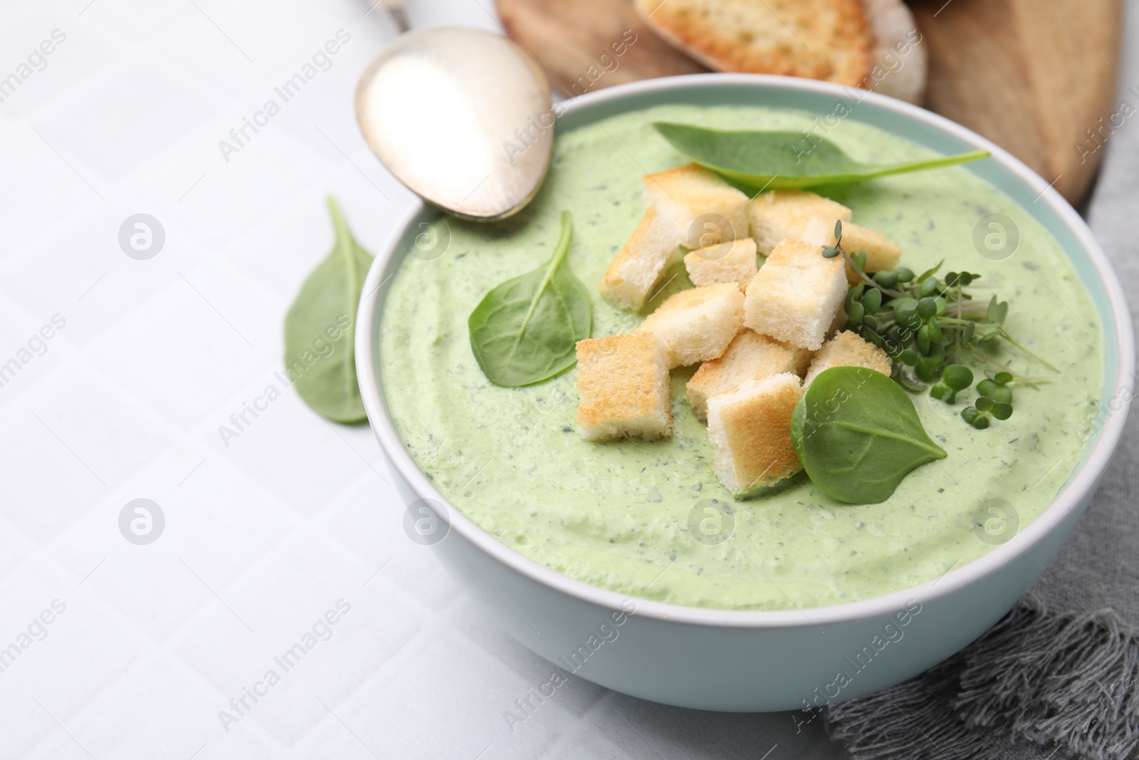 Photo of Delicious spinach cream soup with croutons in bowl on white tiled table, closeup