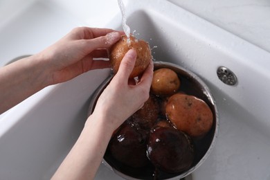 Photo of Woman washing fresh potato in kitchen sink, closeup. Cooking vinaigrette salad