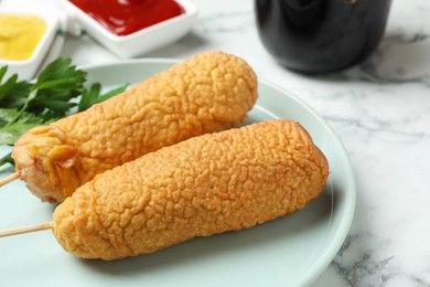 Photo of Delicious deep fried corn dogs on white marble table, closeup