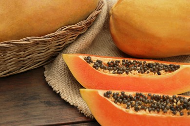 Photo of Tasty whole and cut papaya fruits on wooden table, closeup