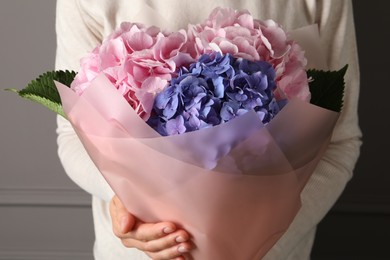 Woman with bouquet of beautiful hortensia flowers near grey wall, closeup