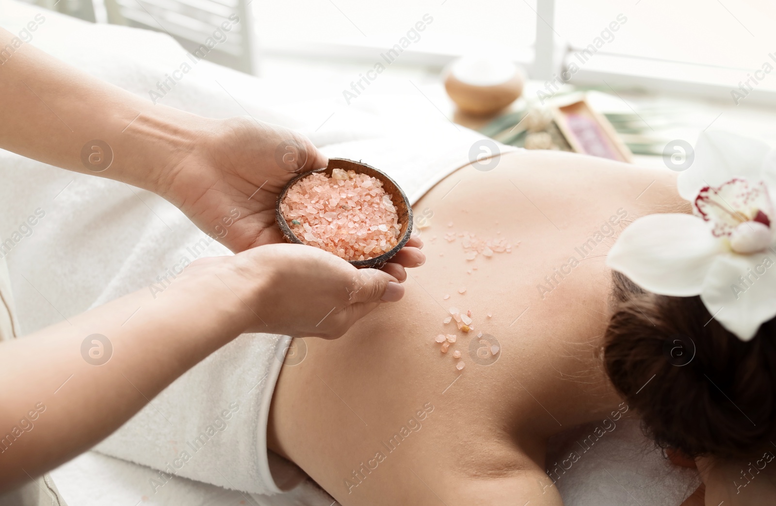 Photo of Young woman having body scrubbing procedure with sea salt in spa salon