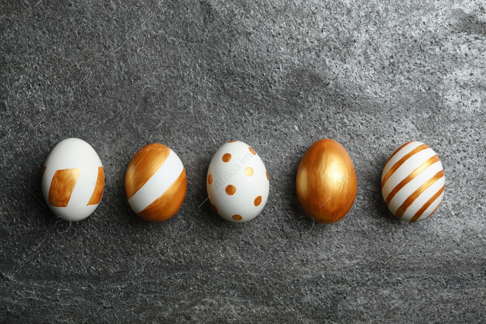 Photo of Set of traditional Easter eggs decorated with golden paint on grey background, top view