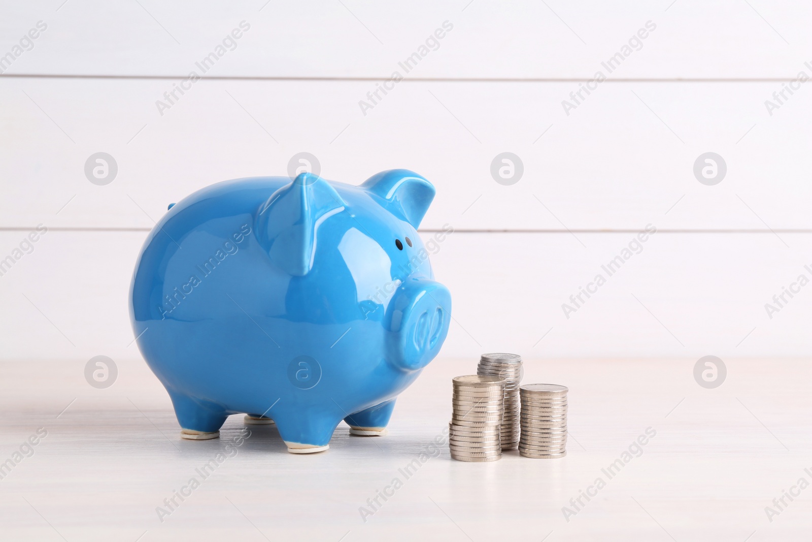 Photo of Financial savings. Piggy bank and stacked coins on white wooden table