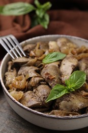 Delicious fried chicken liver with onion and basil in bowl on wooden table, closeup