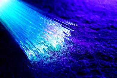 Image of Optical fiber strands transmitting different color light on textured background, closeup. Space for text