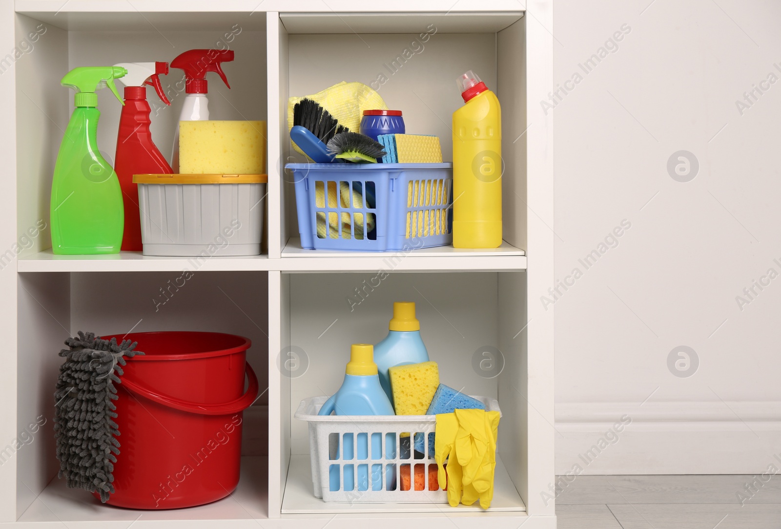 Photo of Shelving unit with detergents and cleaning tools near white wall indoors