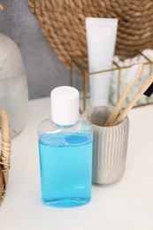 Photo of Bottle of mouthwash and toothbrushes on white table in bathroom