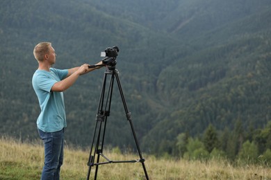 Photo of Photographer taking video with modern camera on tripod in mountains