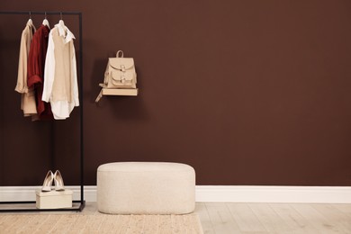 Photo of Stylish ottoman and rack with clothes in hallway. Space for text