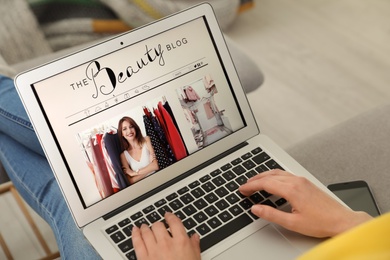 Photo of Woman holding laptop with open beauty blogger site on sofa, closeup
