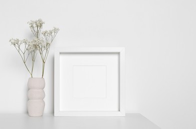 Photo of Empty photo frame and vase with dry decorative gypsophila flowers on white table. Mockup for design