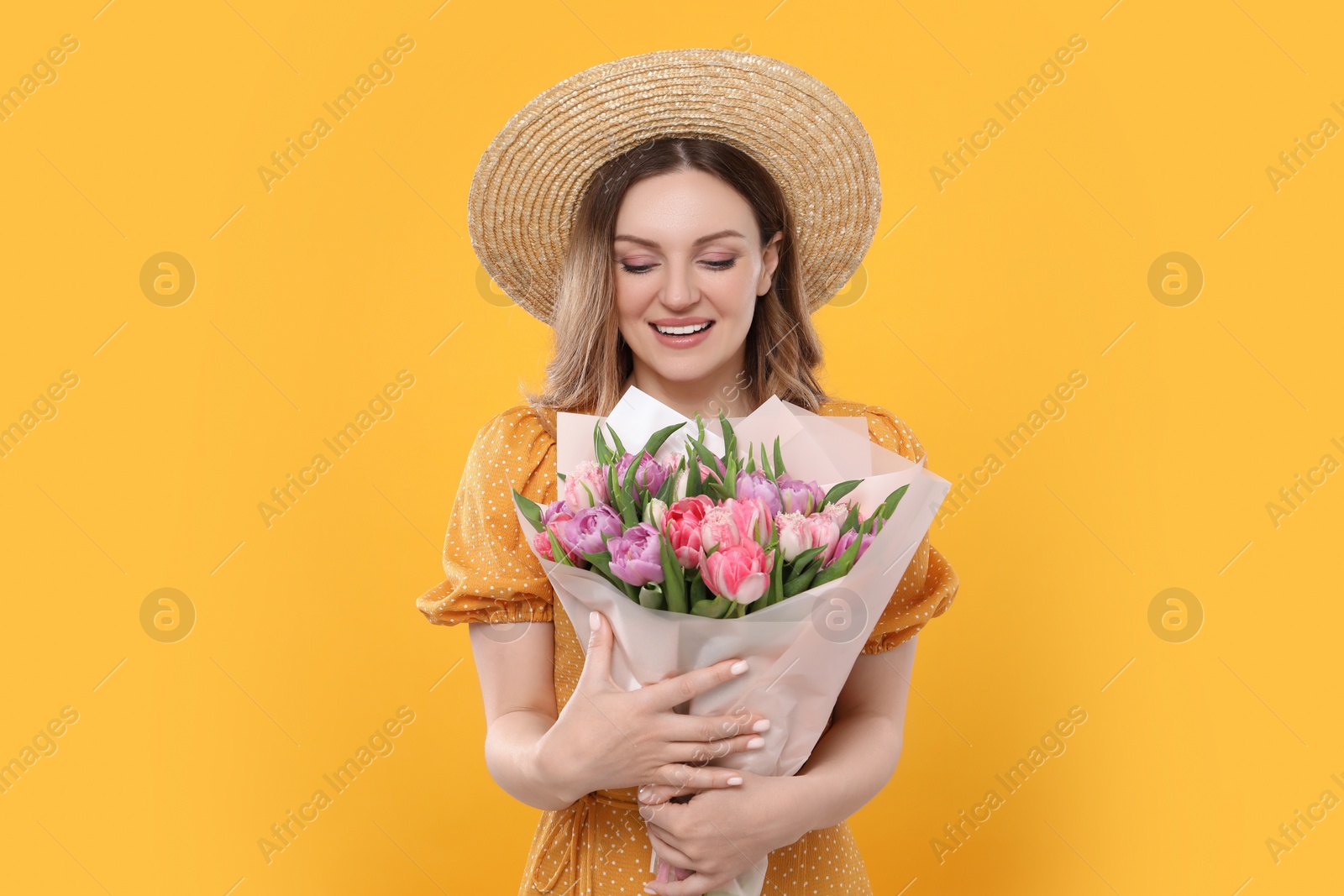 Photo of Happy young woman in straw hat holding bouquet of beautiful tulips on yellow background
