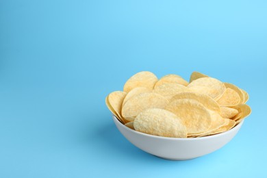 Bowl of tasty potato chips on light blue background, space for text