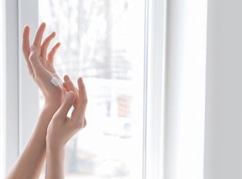 Photo of Young woman applying hand cream against window