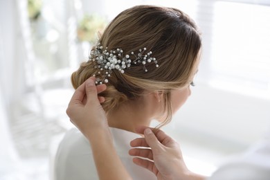 Photo of Professional stylist making wedding hairstyle for bride in salon, back view