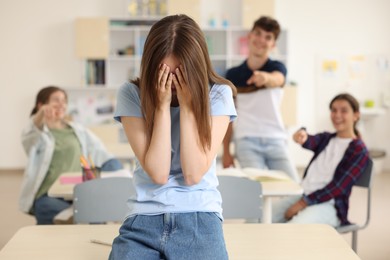 Photo of Teen problems. Students pointing at upset girl in classroom, selective focus