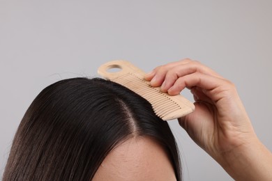 Photo of Woman with comb examining her hair and scalp on grey background, closeup