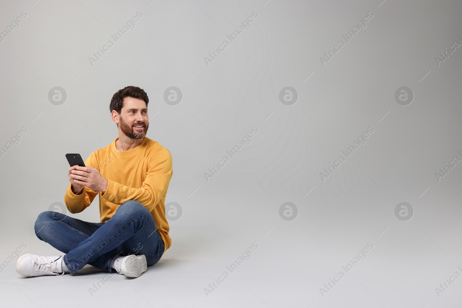 Photo of Smiling man with smartphone on grey background. Space for text