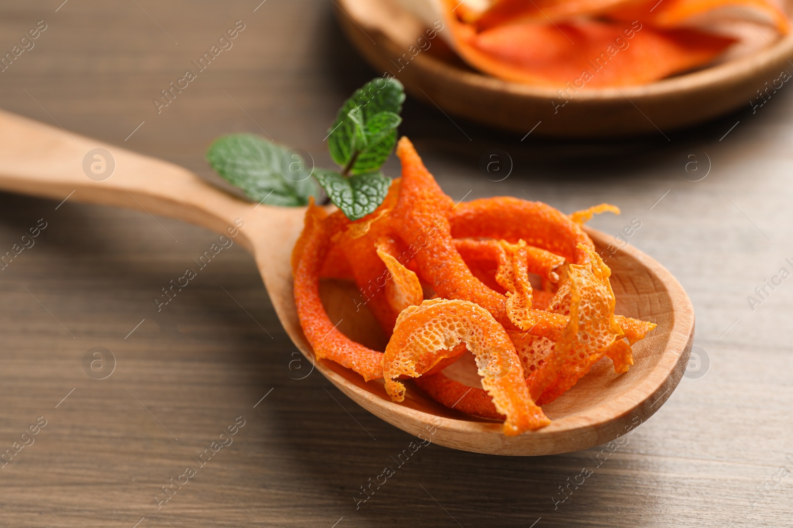 Photo of Spoon with dry orange peels on wooden table, closeup