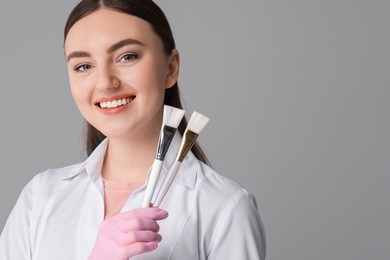 Photo of Cosmetologist with cosmetic brushes on grey background, space for text