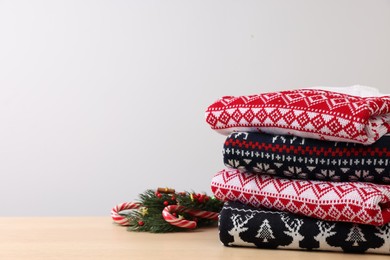 Stack of different Christmas sweaters and decor on table against light background. Space for text