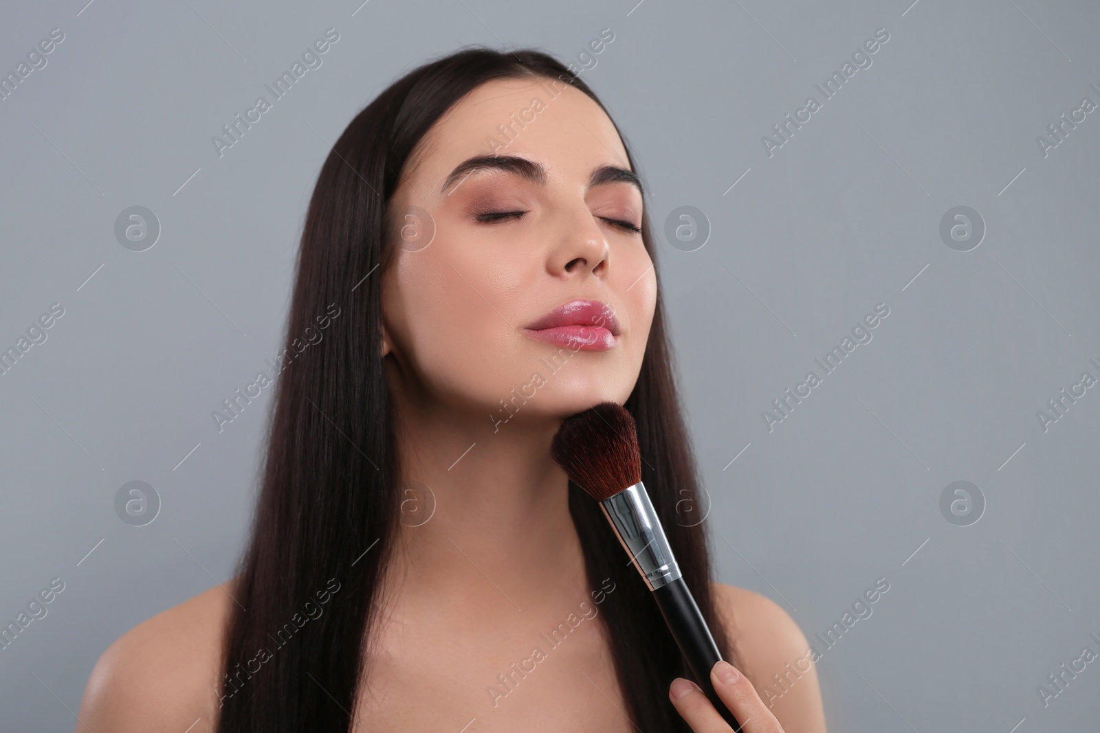 Photo of Beautiful woman with makeup brush on light grey background