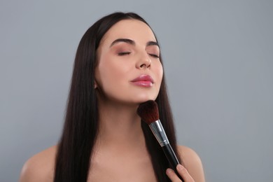 Beautiful woman with makeup brush on light grey background