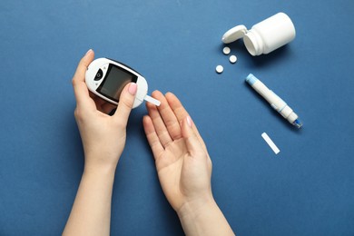 Diabetes. Woman checking blood sugar level with glucometer on blue background, top view