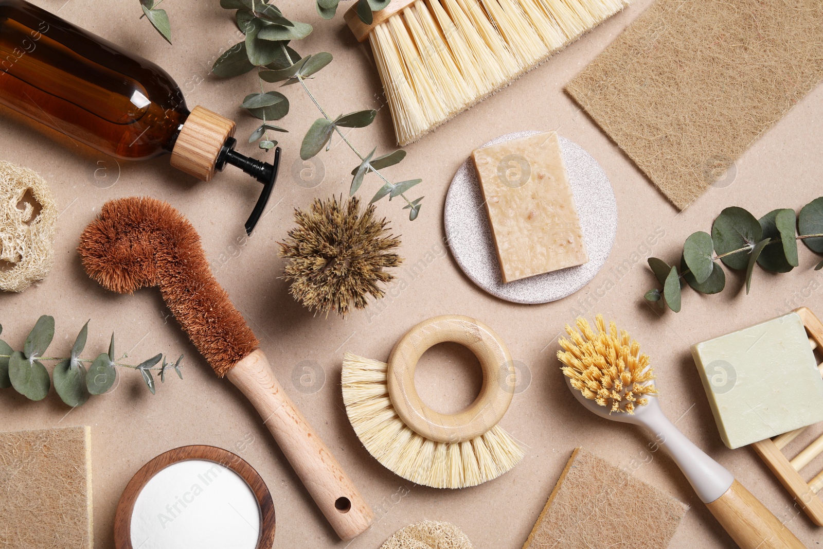 Photo of Cleaning brushes, baking soda, soap, sponges and eucalyptus leaves on pale brown background, flat lay