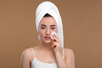 Photo of Beautiful woman in terry towel removing makeup with cotton pad on beige background