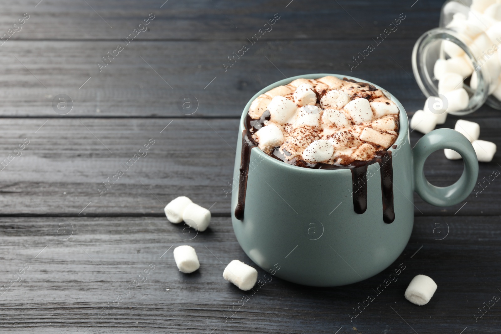 Photo of Cup of aromatic hot chocolate with marshmallows and cocoa powder on dark gray wooden table, closeup. Space for text