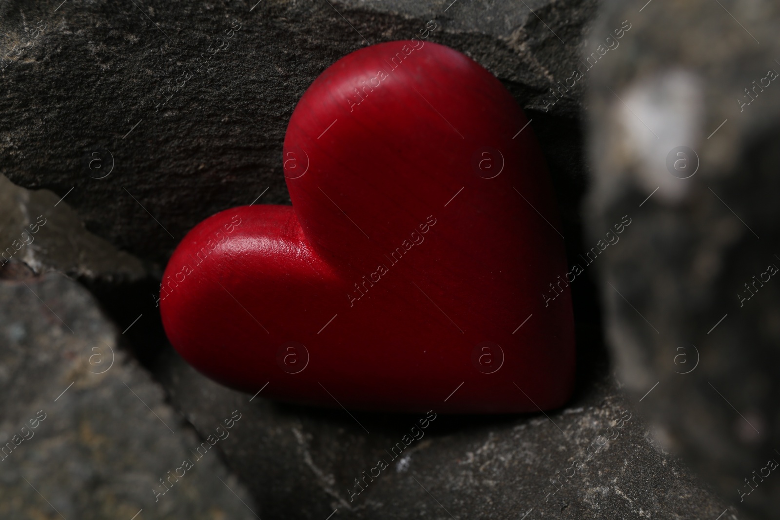 Photo of One red decorative heart between stones, closeup