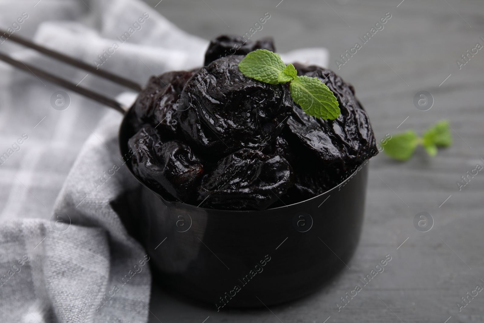 Photo of Sweet dried prunes and mint in scoop on grey wooden table, closeup