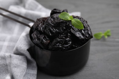 Photo of Sweet dried prunes and mint in scoop on grey wooden table, closeup