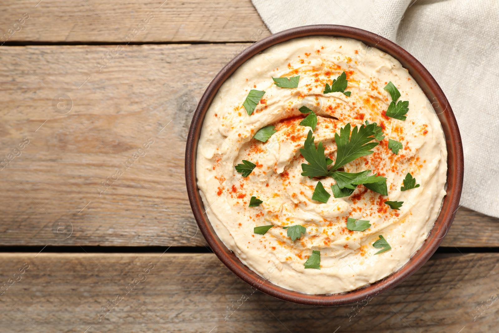 Photo of Tasty hummus with parsley and paprika in bowl on wooden table, top view. Space for text