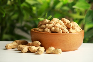 Fresh unpeeled peanuts in bowl on white table against blurred background