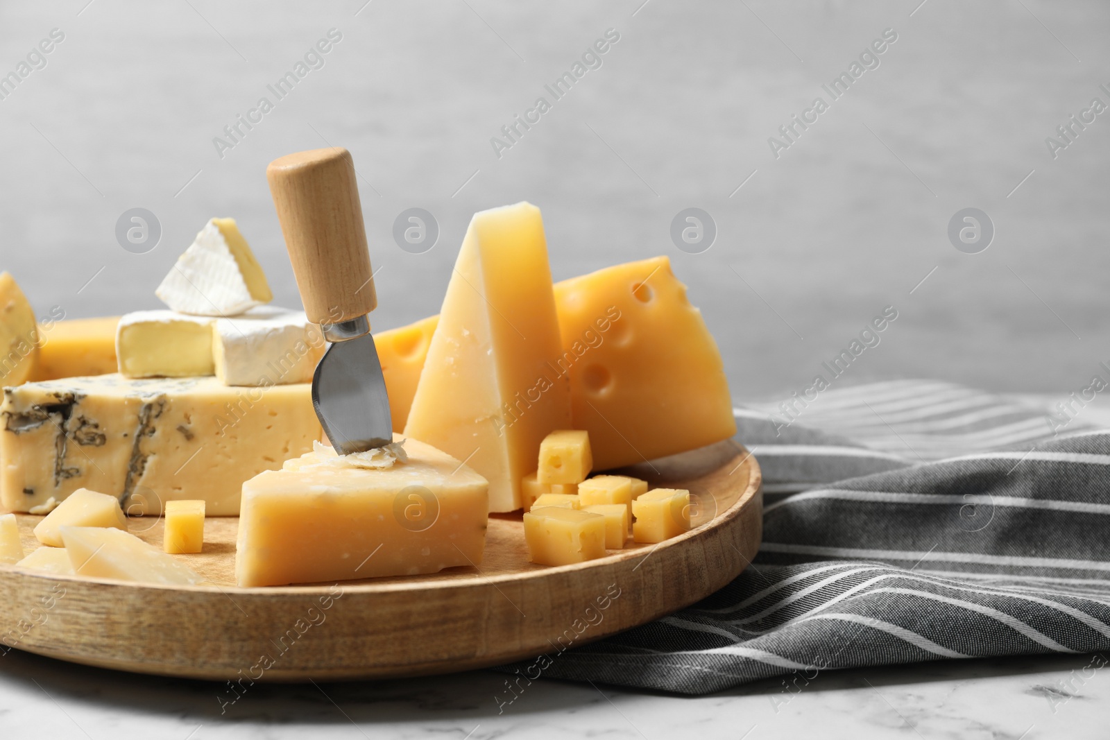 Photo of Different types of delicious cheese in plate on marble table against light background, space for text