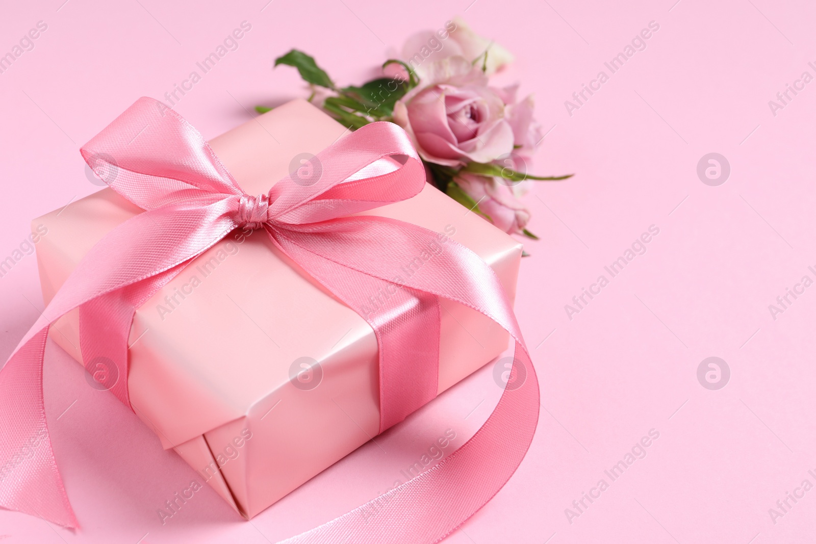Photo of Gift box and beautiful rose flowers on pink background, closeup