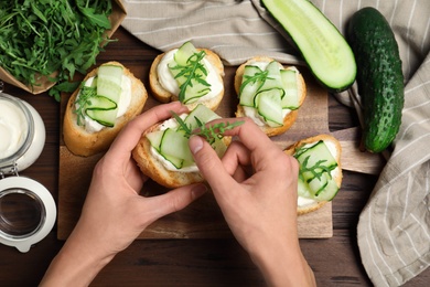 Woman preparing bruschetta with cucumbers at wooden table, top view