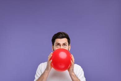Photo of Man inflating red balloon on purple background. Space for text