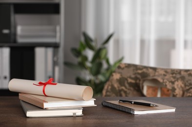 Photo of Diploma, notebooks and pen on wooden table indoors. Military education