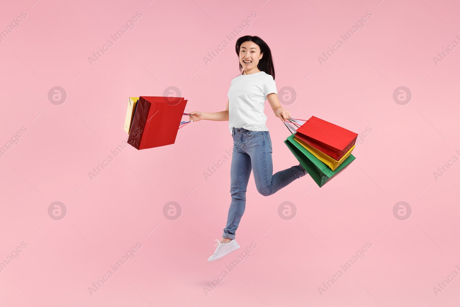 Photo of Happy woman with shopping bags jumping on pink background