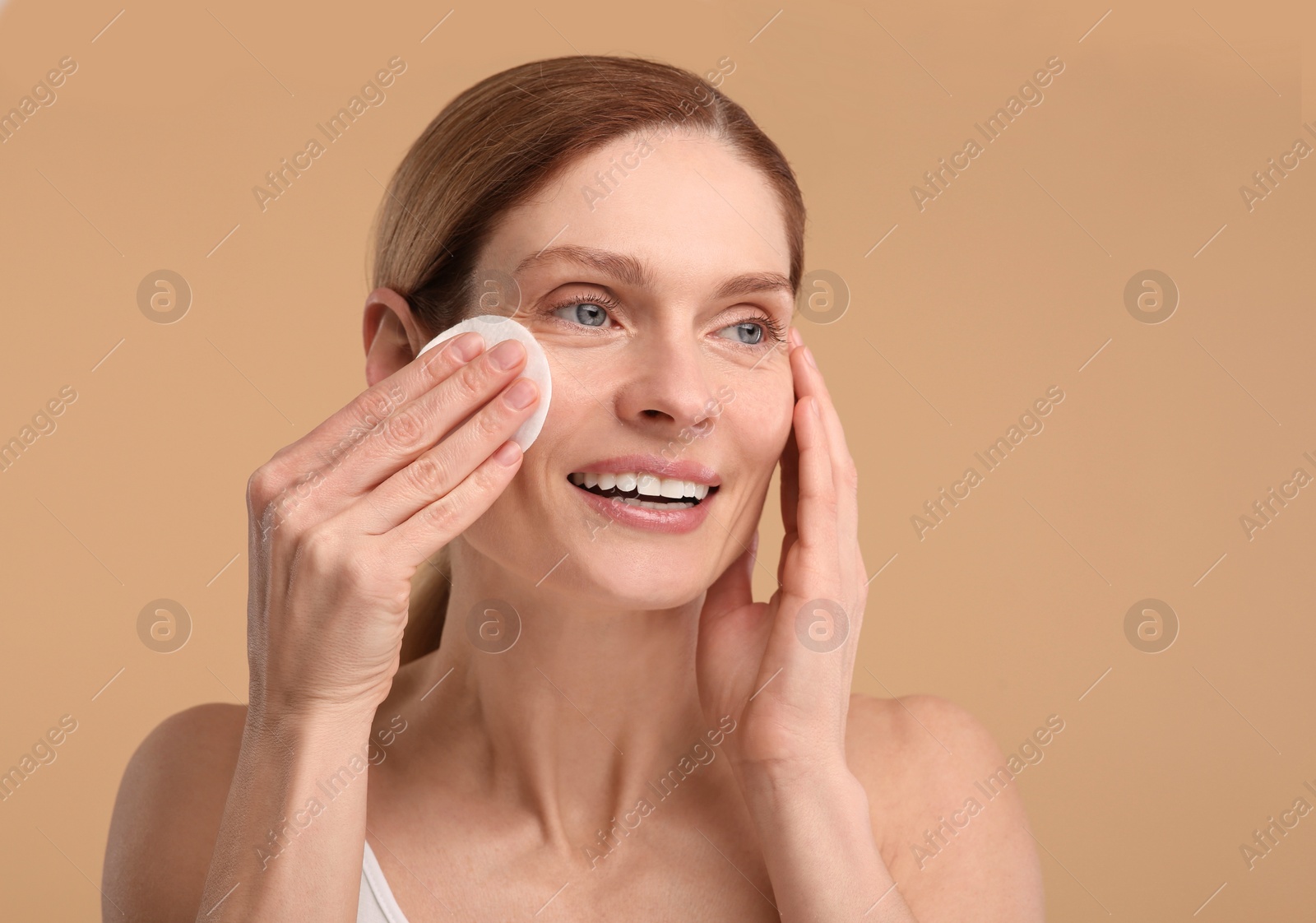 Photo of Beautiful woman removing makeup with cotton pad on beige background