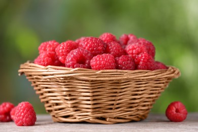 Photo of Wicker basket with tasty ripe raspberries on wooden table against blurred green background, closeup
