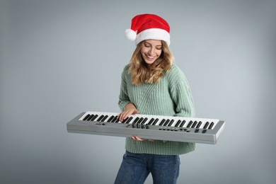 Photo of Young woman in Santa hat playing synthesizer on light grey background. Christmas music