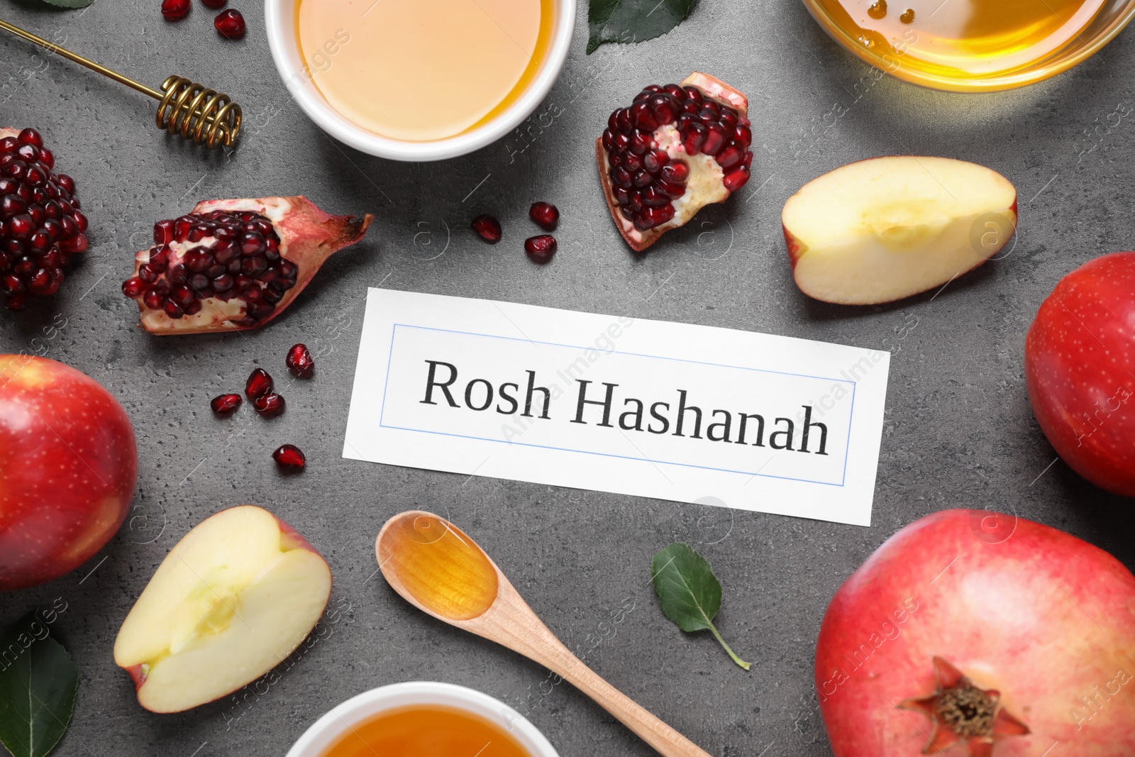 Photo of Card with text ROSH HASHANAH, apples, honey and pomegranates on grey table, flat lay